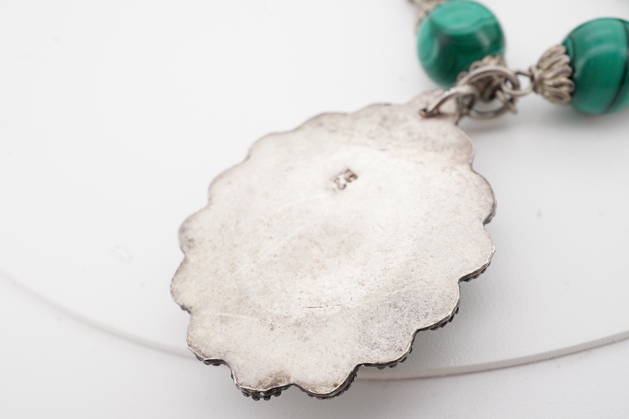 An Arts & Crafts silver and malachite necklace, early 20th century composite, the front composed of malachite beads in silver wire work mounts, suspending a green hardstone pendant in a floral silver border, necklace len